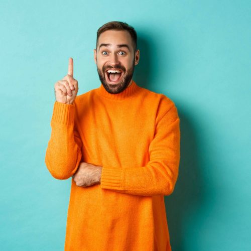 Handsome caucasian man having an idea, raising finger up and saying his plan, standing excited against turquoise background.