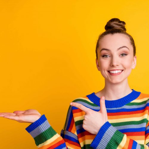 Portrait of positive cheerful promoter girl point index finger copyspace hand recommend choose decide advise promo ads wear sweater isolated over bright color background